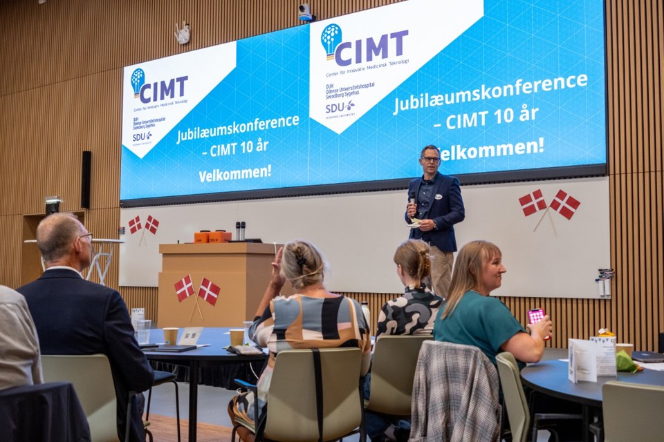 A man on stage in front of slides projected on a screen