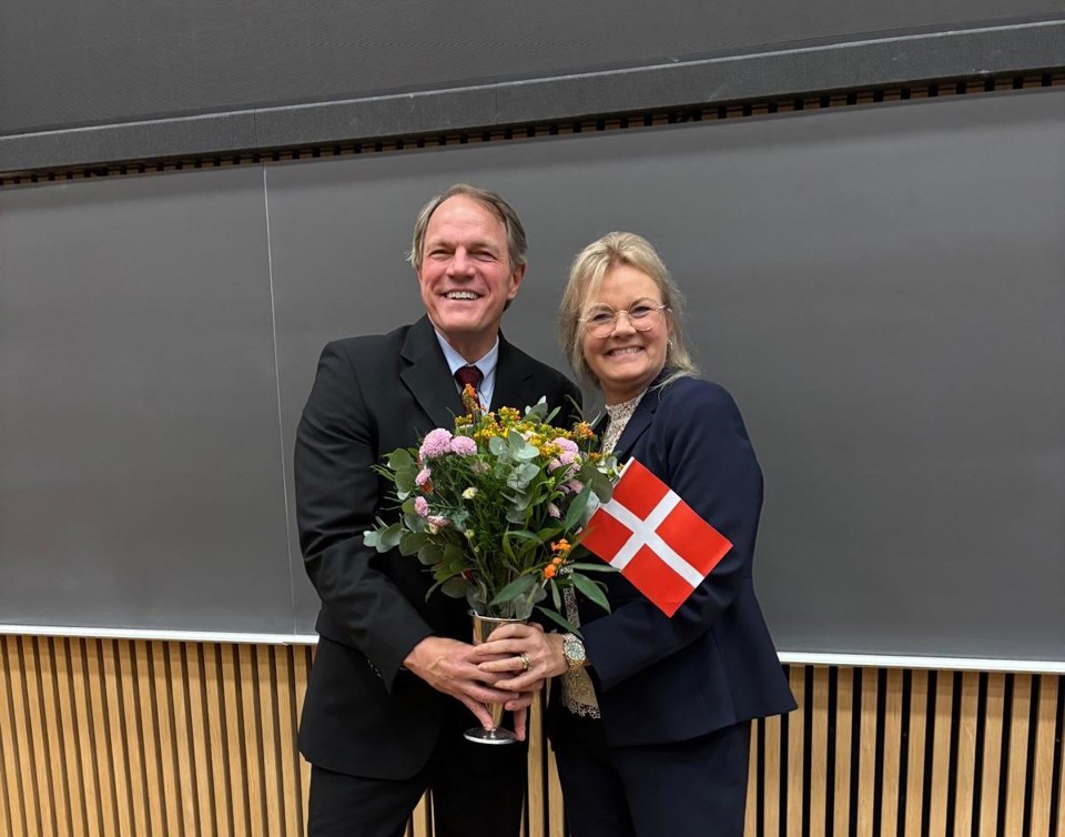 Professors James Marcin and Jane Clemensen holding a bouquet of flowers and a Danish flag
